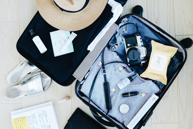 Mala de viagem aberta com roupa, chapéu, máquina fotográfica e artigos de higiene preparados para viajar