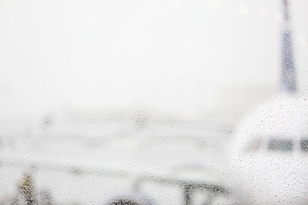 Avião visto através de uma janela do aeroporto com gotas de chuva